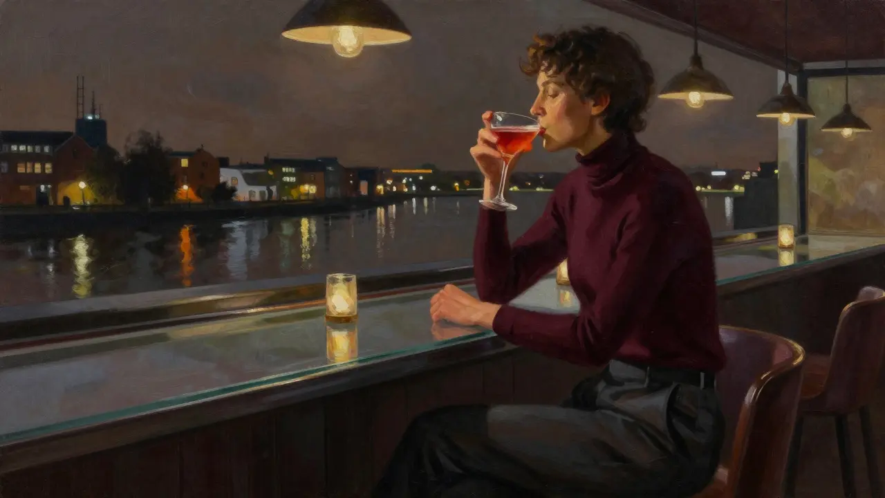 Person at a rooftop bar in Wapping Wharf wearing dark turtleneck and tailored trousers, sipping cocktail with river reflections.