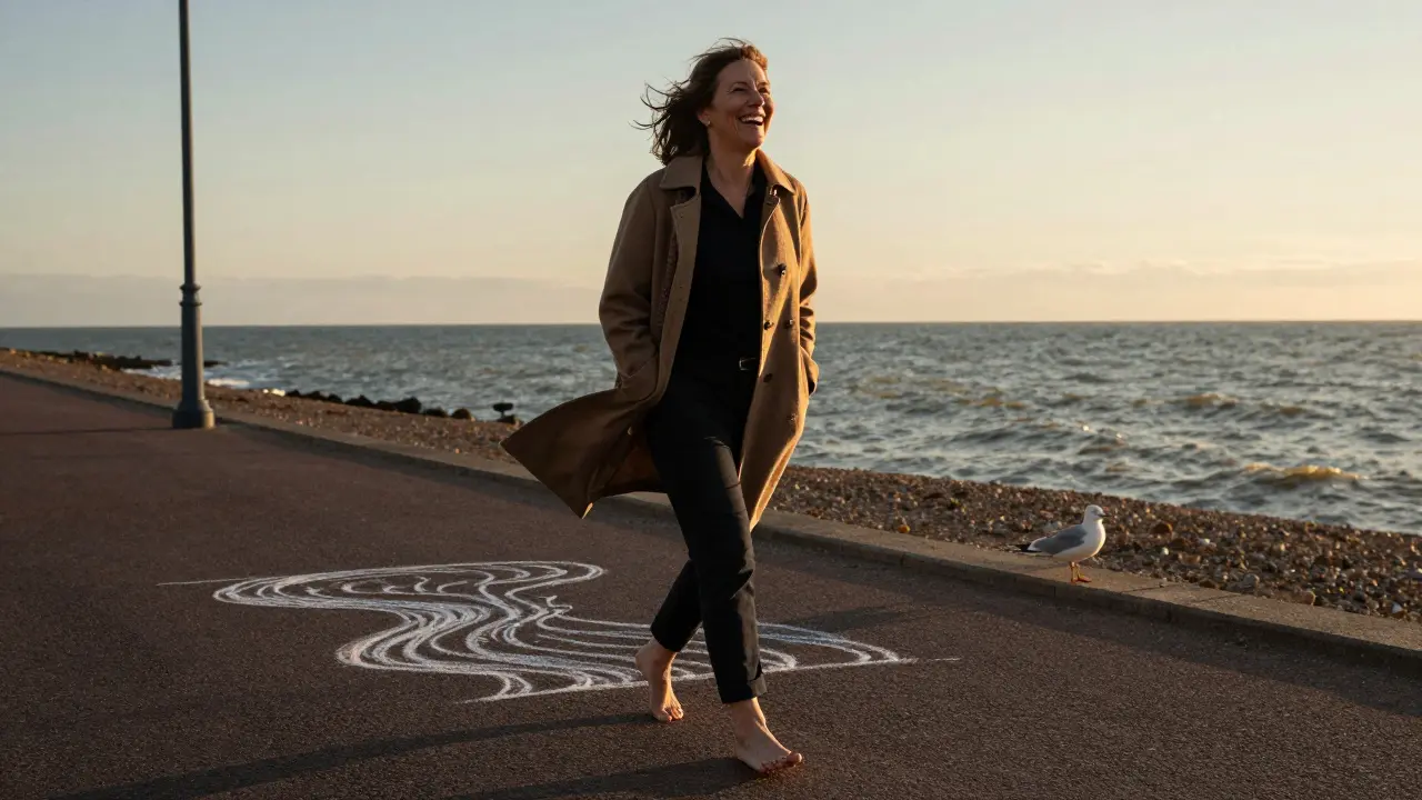 A mature woman laughing as she walks barefoot along the Brighton shore at sunset.